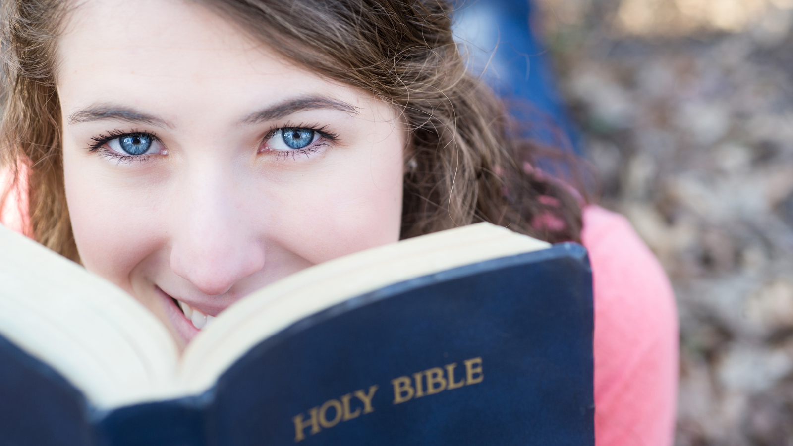 Girl with blue eyes reading her Bible looking at camera
