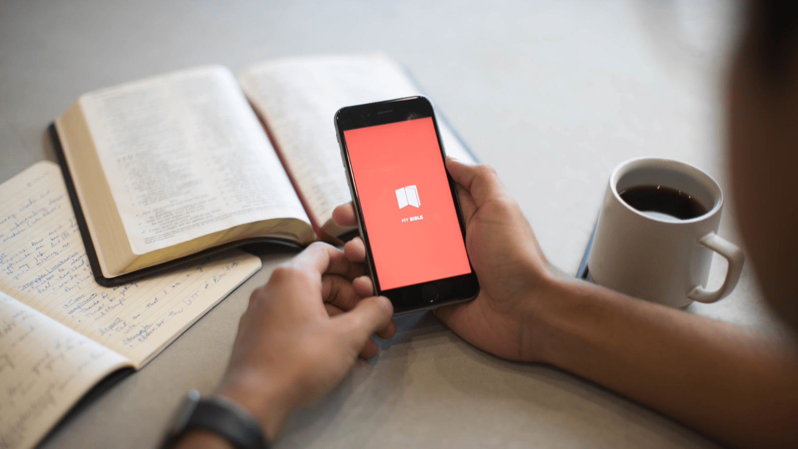 Man's hand holding phone with Bible