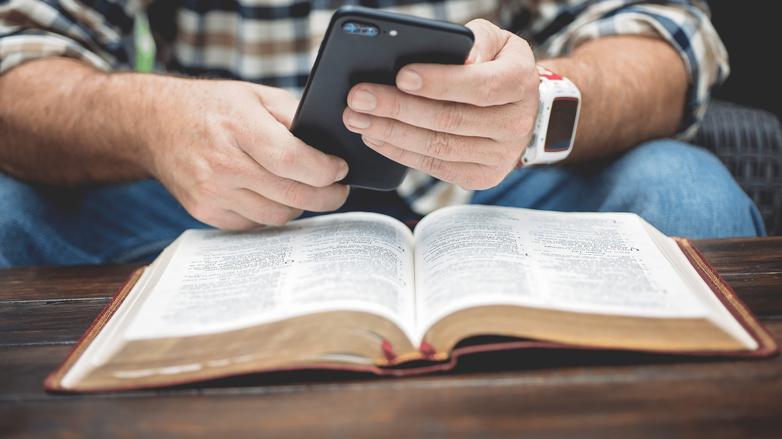 Man looking at phone over Bible