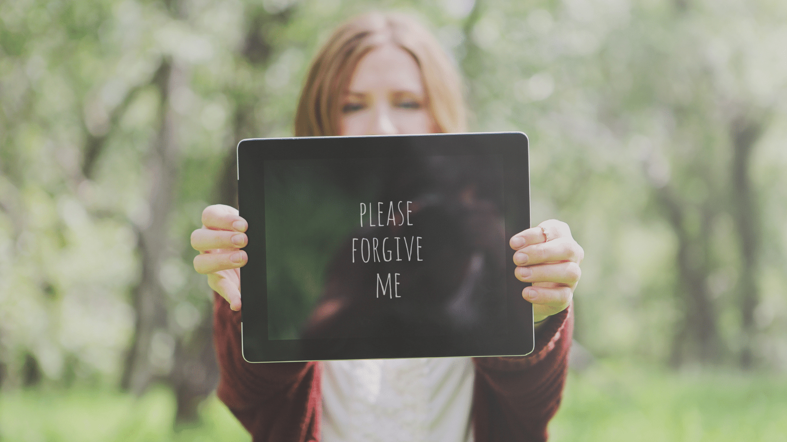 Woman holding sign that says please forgive me.