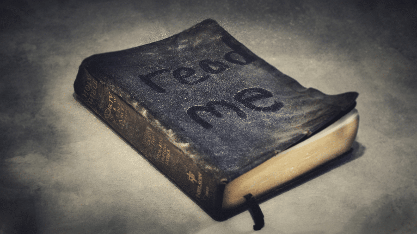 dusty Bible with "read me" written in the dust on the front cover