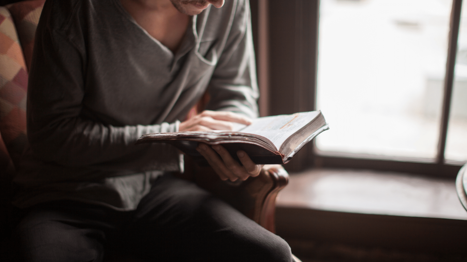 man reading Bible by window