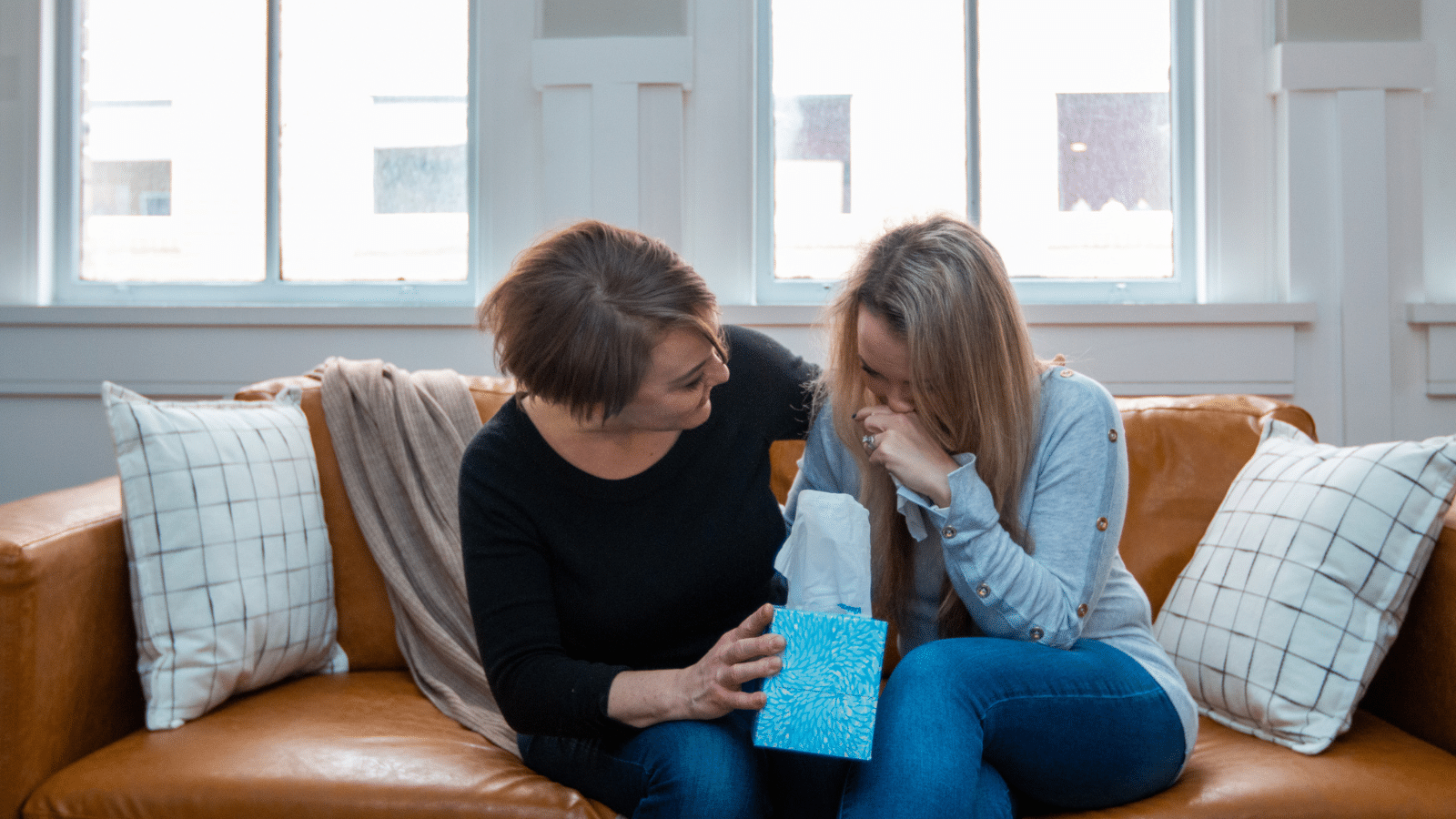 woman offering comfort with box of tissues on couch