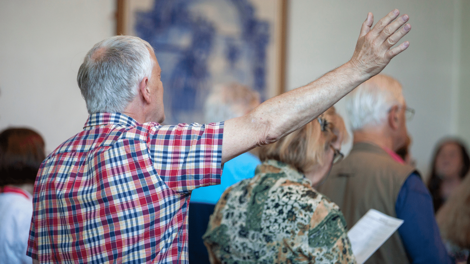 An elderly man with hand raised in praise during a worship service