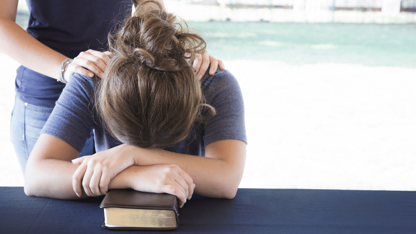 woman with head over Bible while someone prays over her