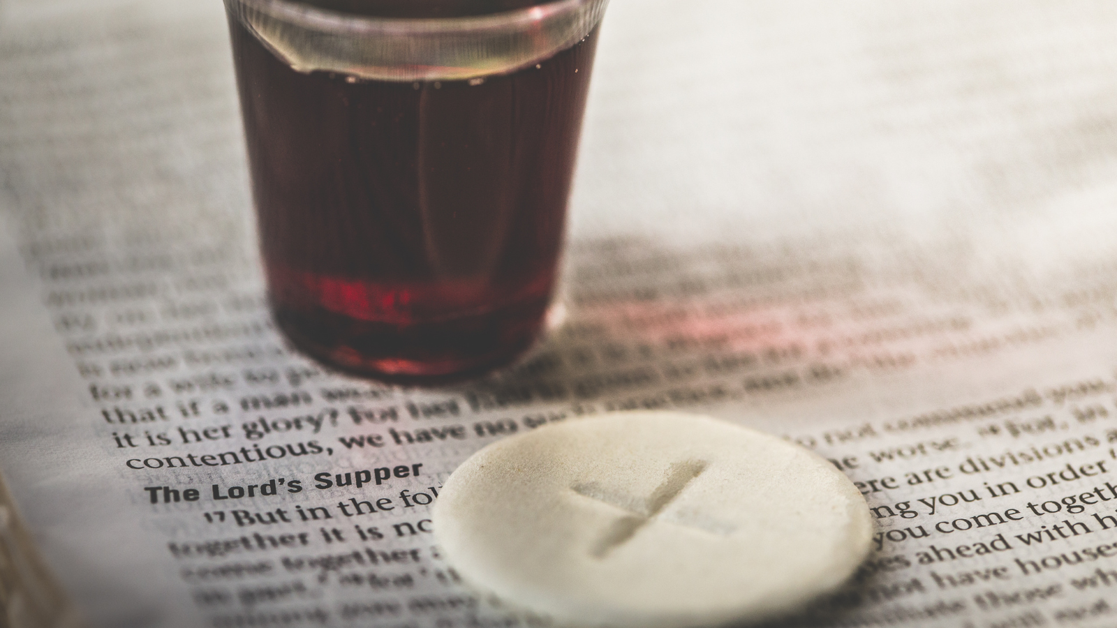 Communion in church showing a glass of red wine and an (Eulogia) bread offering at church, with a cross engraved in the middle, sitting on a Bible, with" in bold print