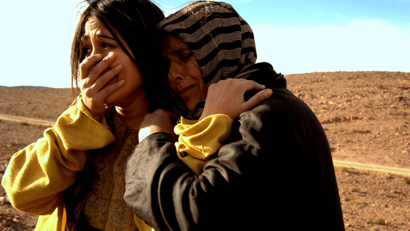 An older Mother hugging her daughter from behind, as she cries in sadness.