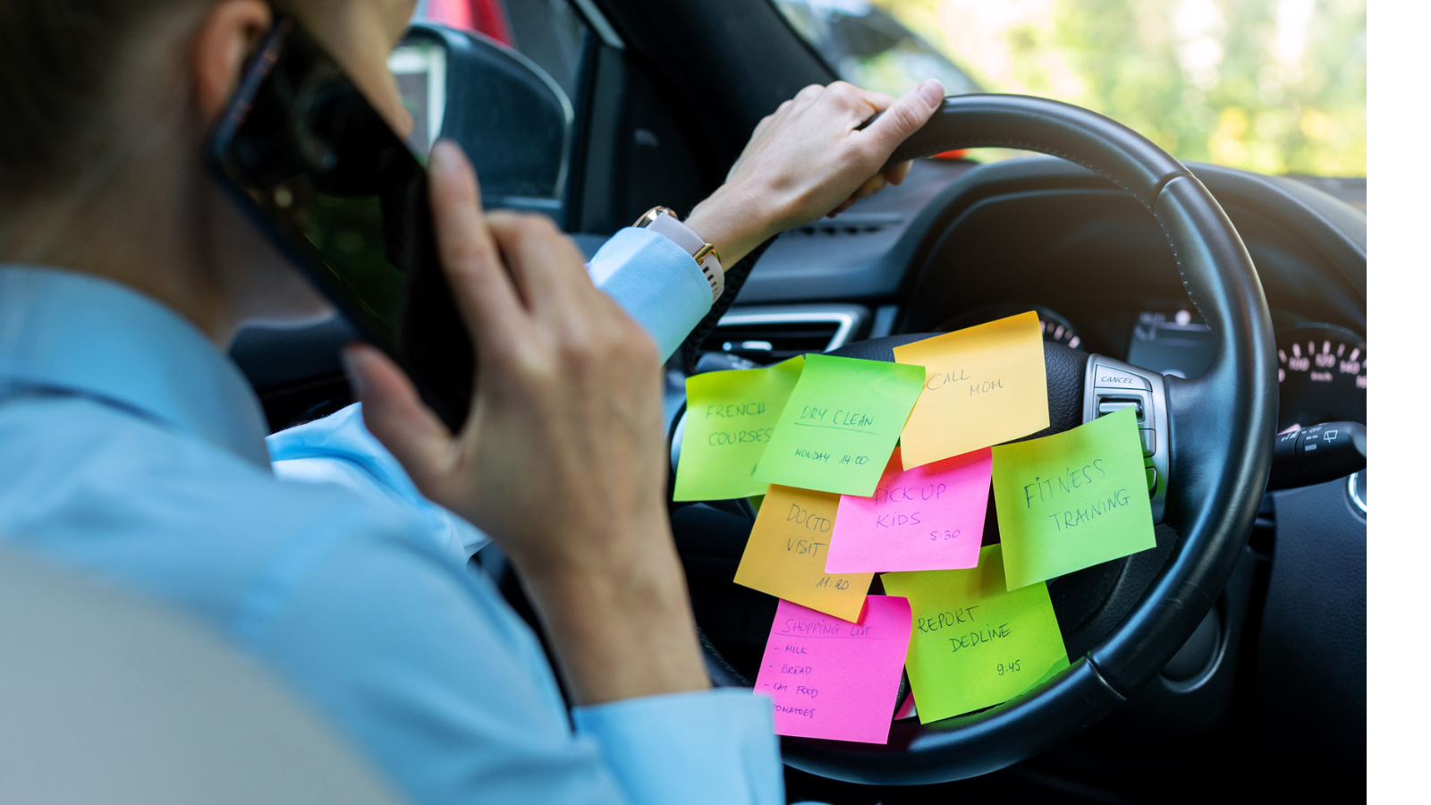 A woman on the phone while driving in her car, with multiple color sticky notes on the steering wheel representing everything she has to do.