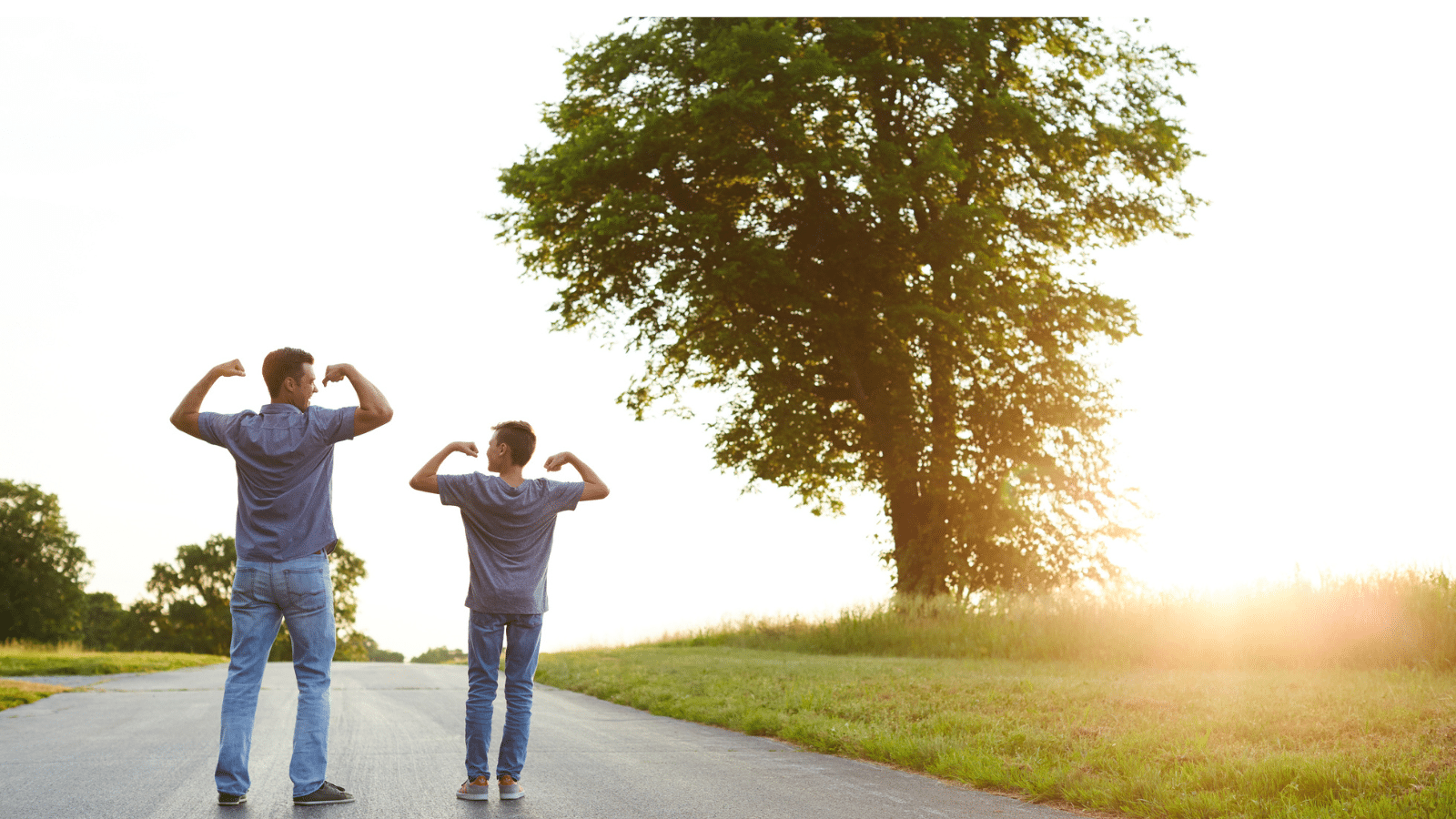 Father and Son walking down a paved road next to a tree, with arms up both showing their muscles (strength).