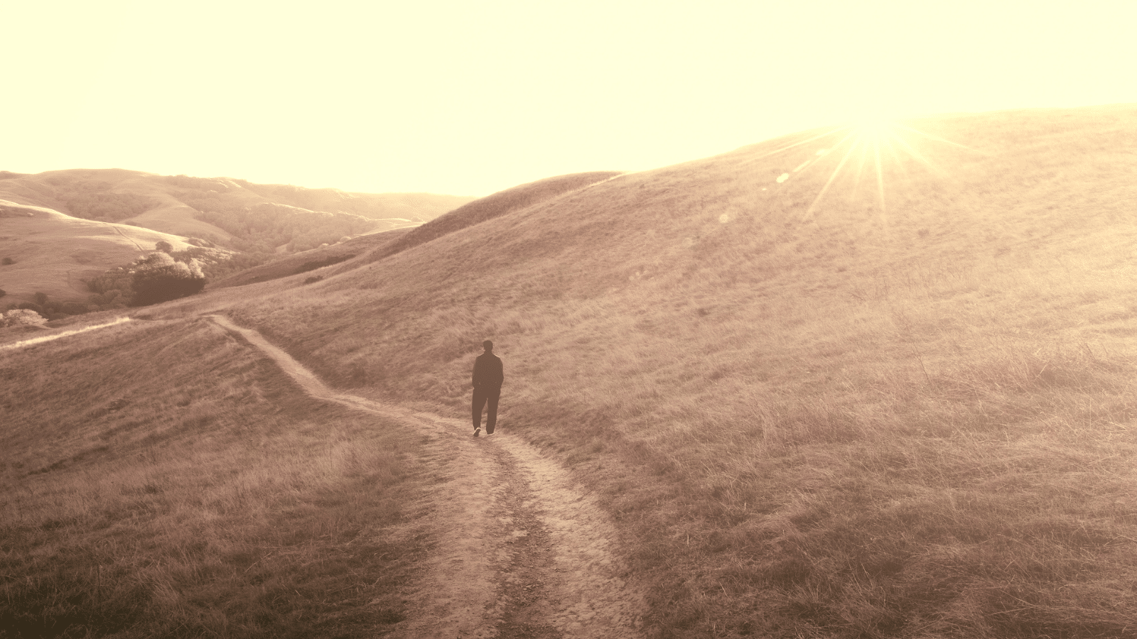 A man walking on a path on a mountainside, at sunset.