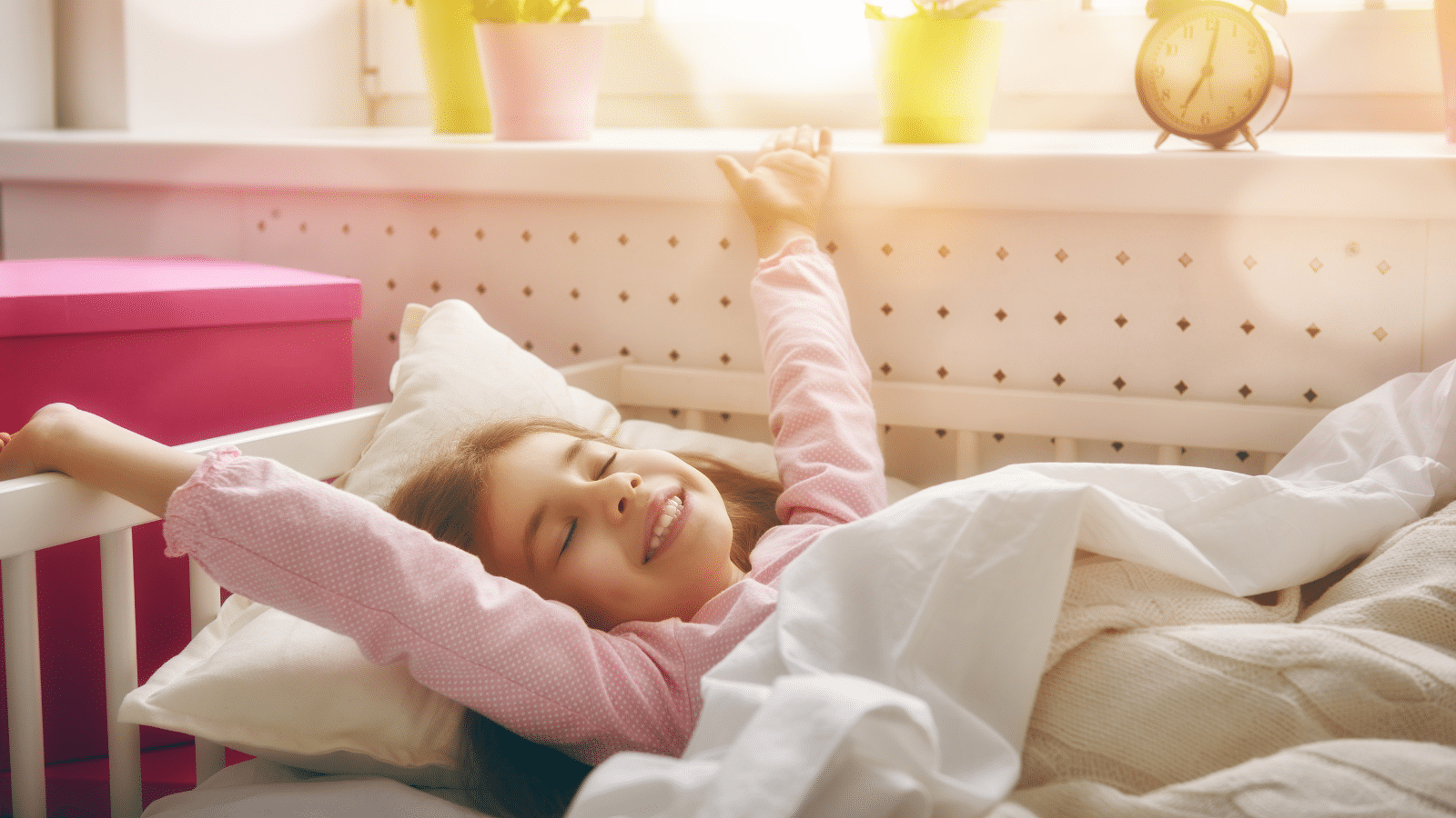 Little girl stretching in her bed as she wakes up to the sun shining on her.