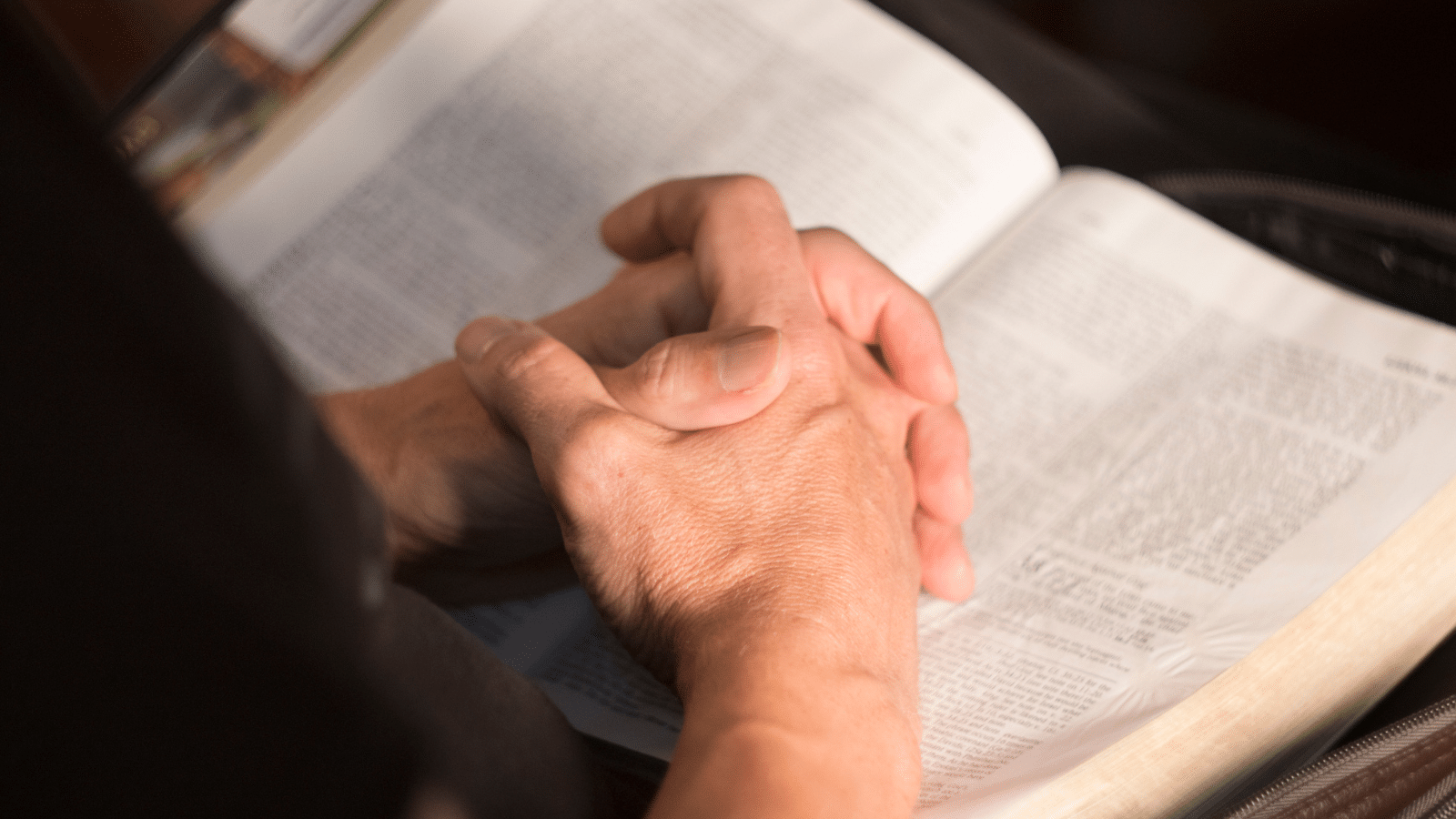 folded hands on Bible