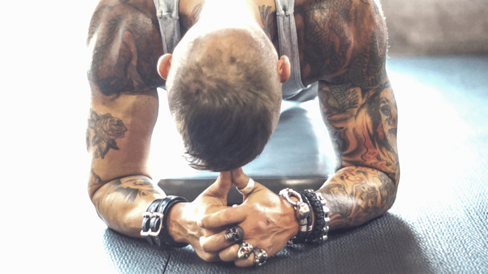 man with lots of tattoos bowing in prayer