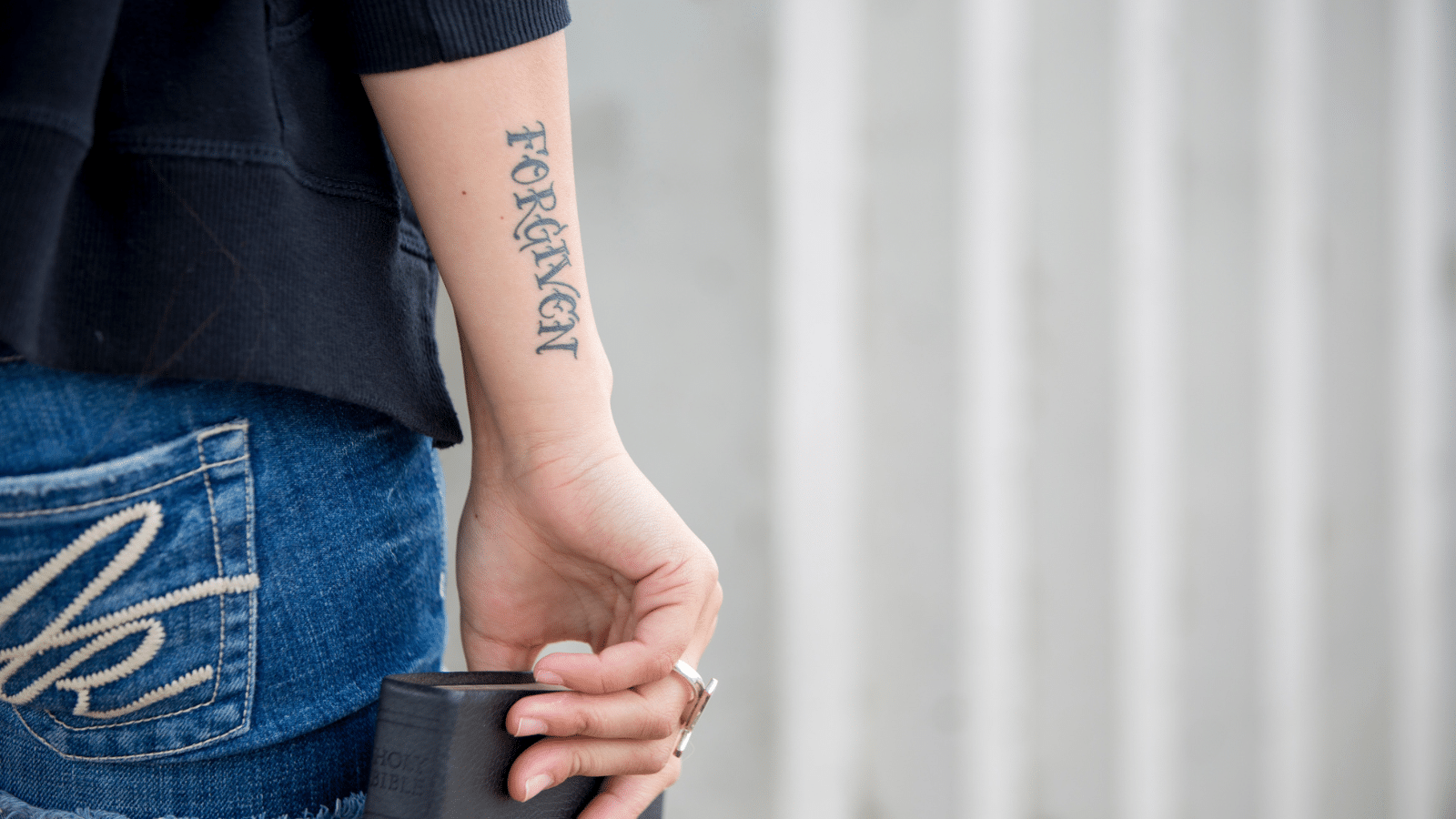 woman holding Bible with forgiven tattoo