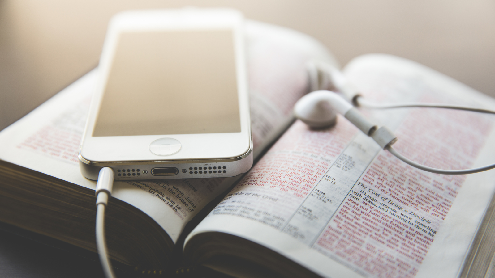 An iphone with earbuds on top of an open bible.