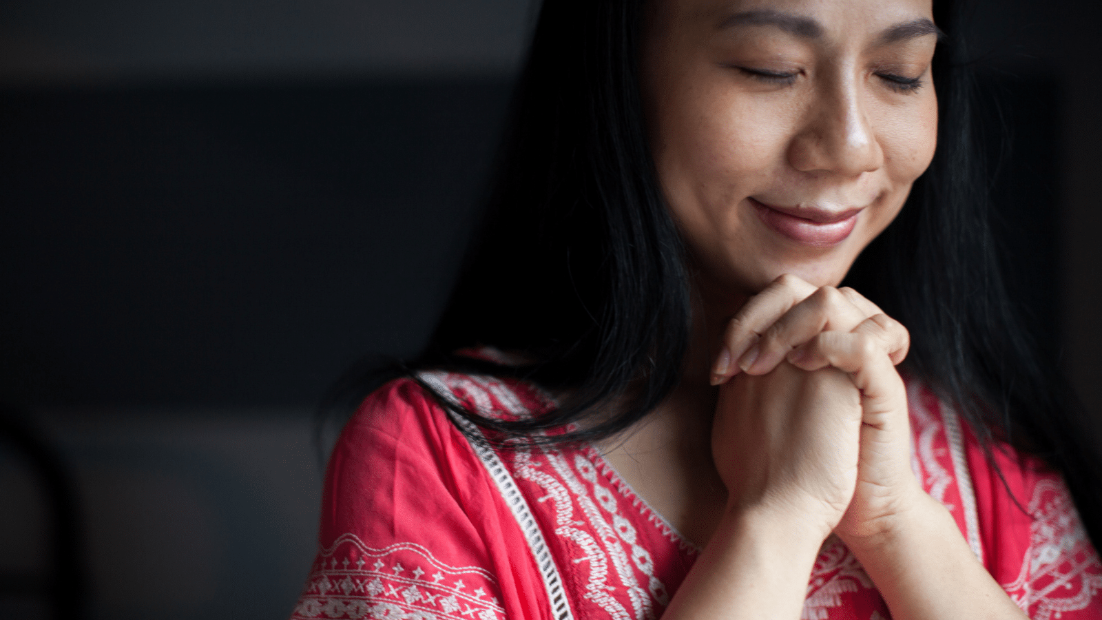 A woman in a red shirt praying.