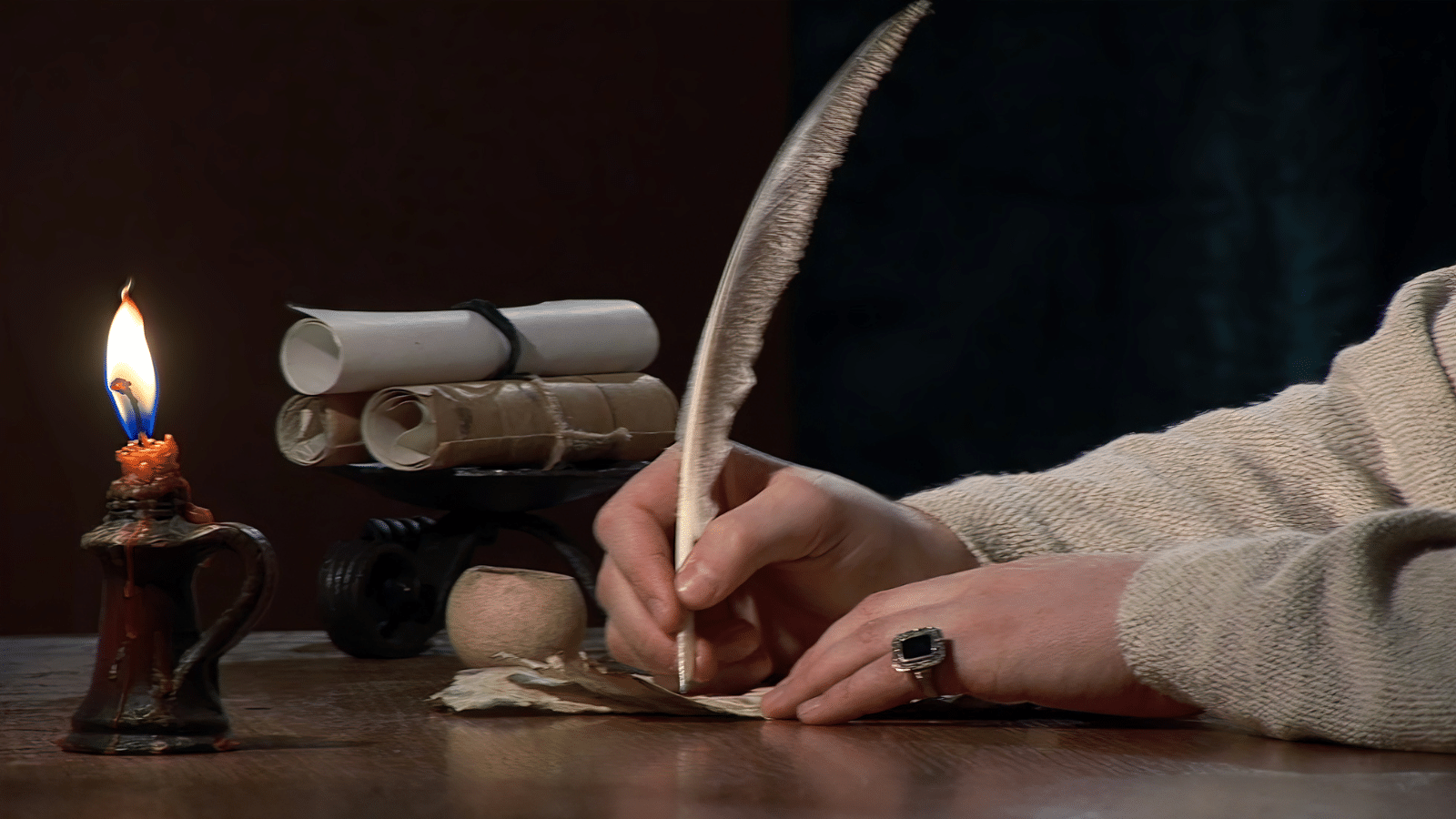 Hands writing a letter with a feather pen.