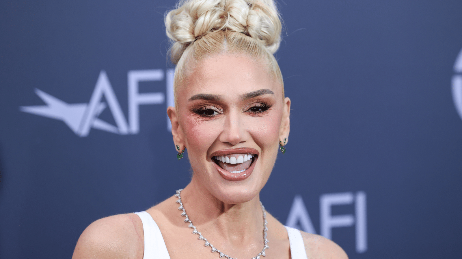 Gwen Stephani with an updo standing in front of a blue background.