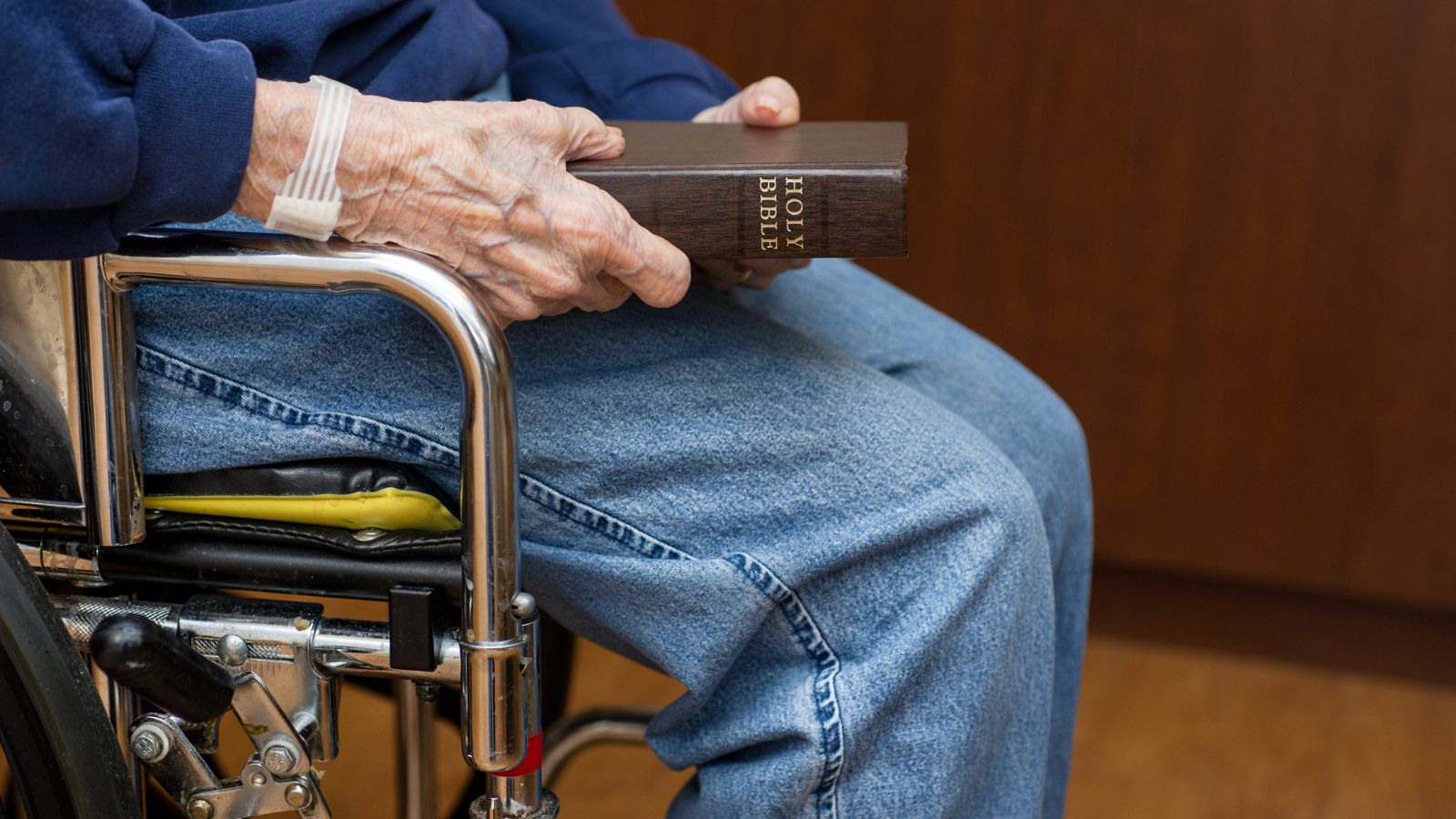 An elderly man in a wheelchair holding a bible.