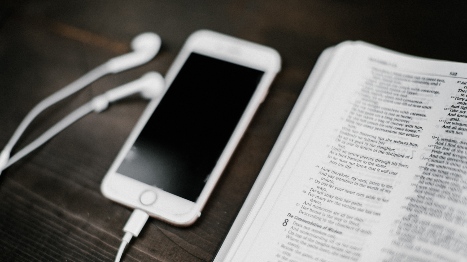 An iphone with earbuds next to an open bible.