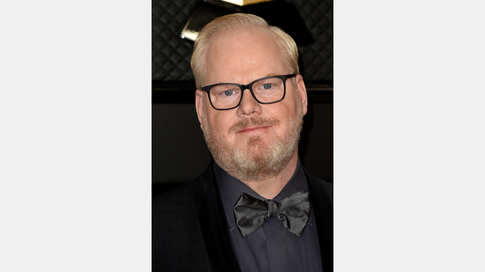 Jim Gaffigan standing in front of a black background.