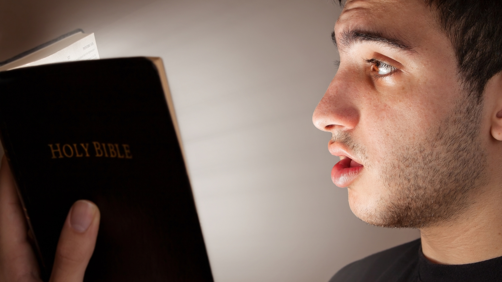 A man reading a bible looking surprised.