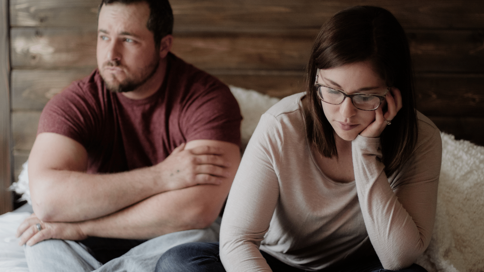 A couple on a bed looking upset.