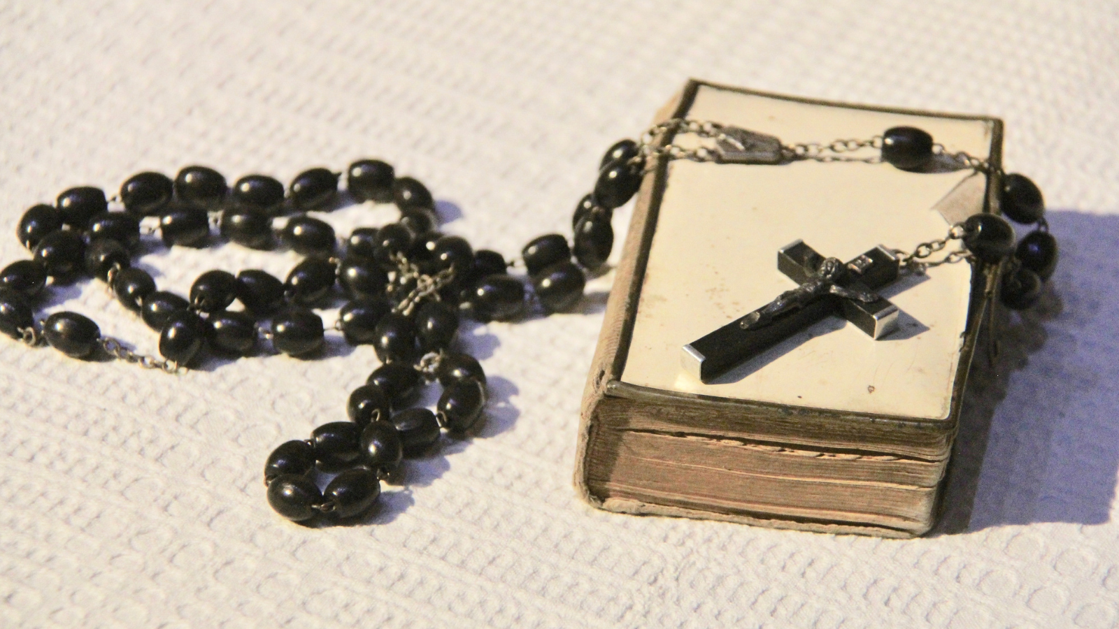 A closed book with a black rosary strewn across it.