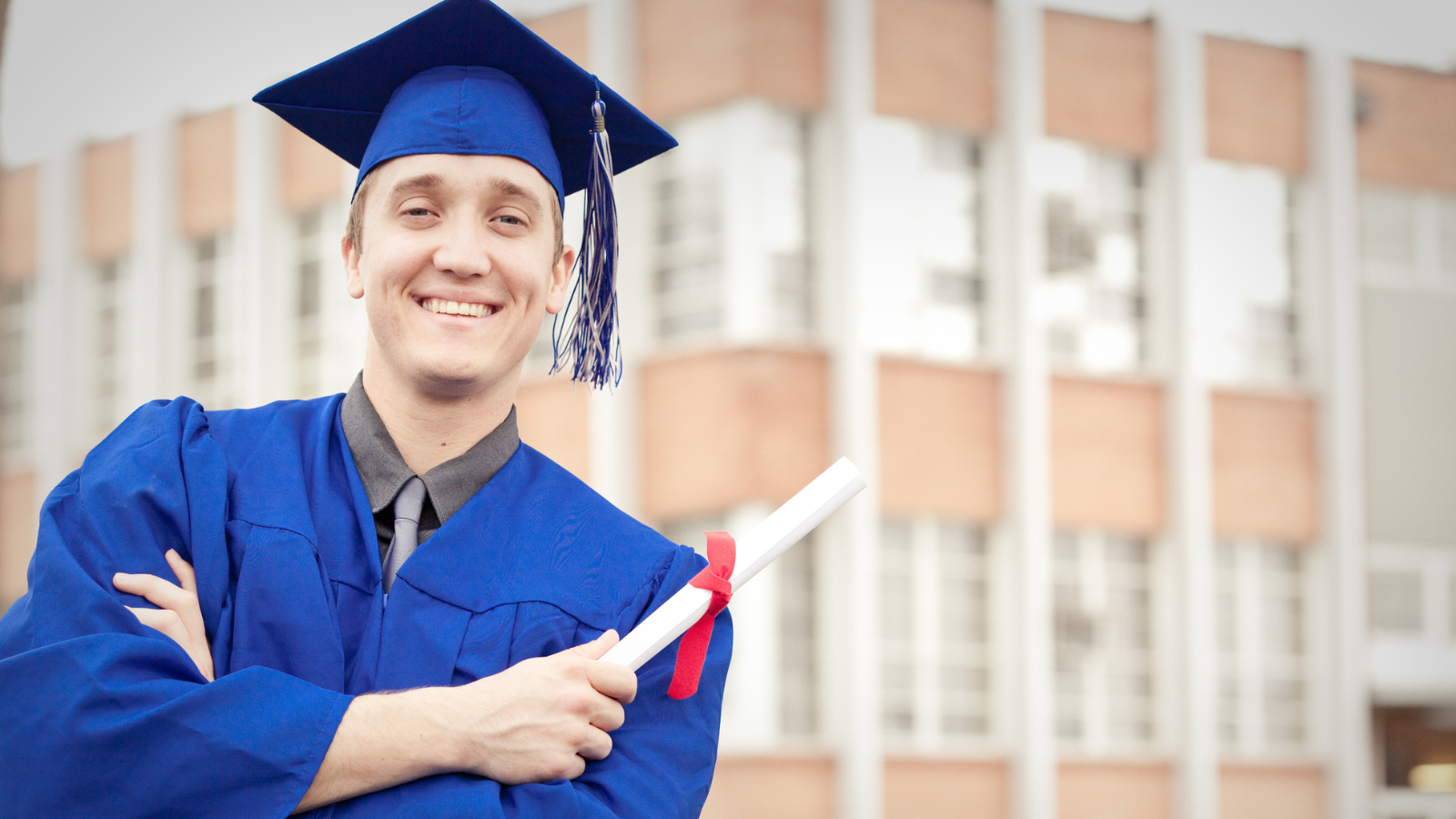 A man wearing a blue graduation gown and holding a diploma.