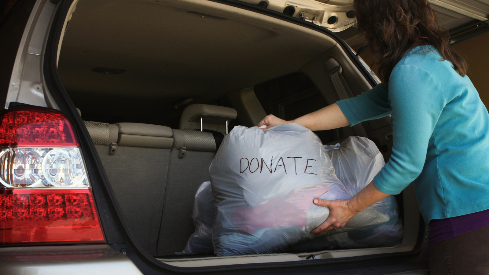 A woman placing a donation bag in her trunk.