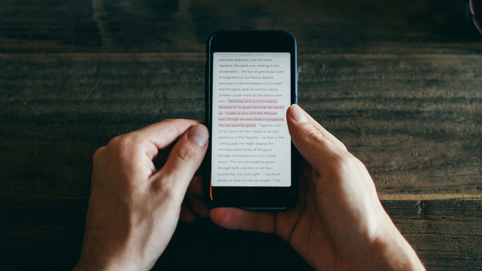 Hands holding a phone with scripture text on the screen.