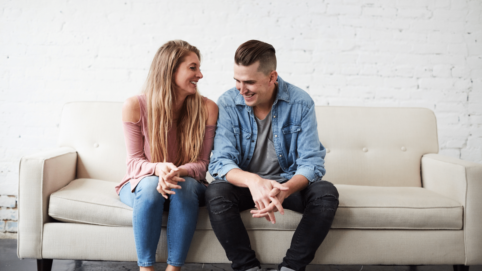 A man and a woman sitting on a couch smiling.