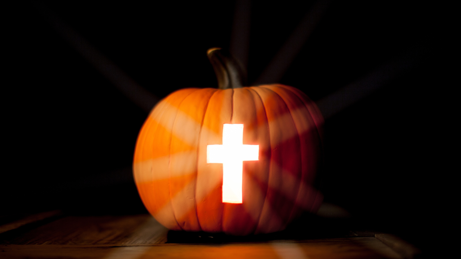 A cross carved into a lit up pumpkin.
