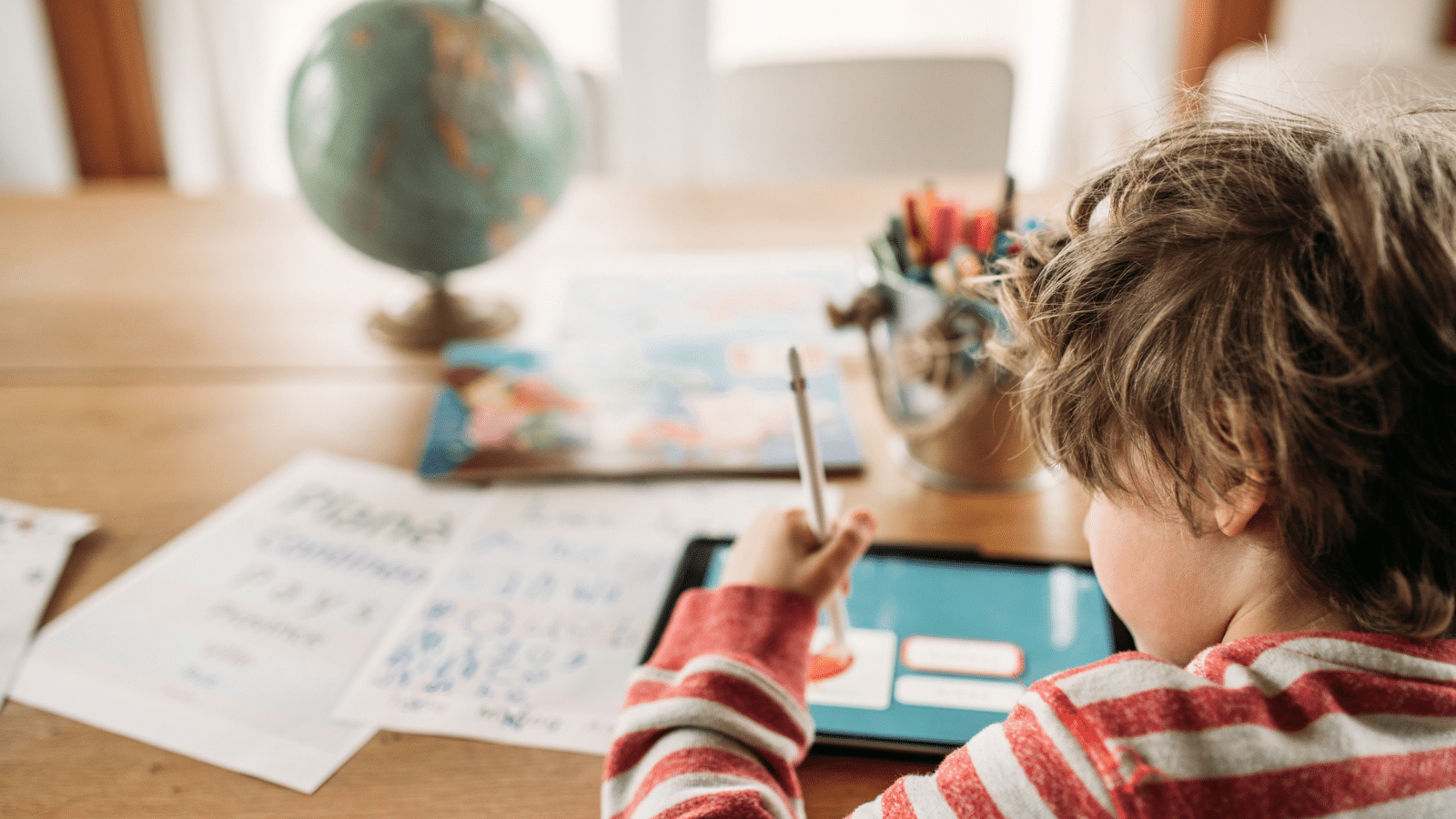 A boy sitting at a table working on a tablet.