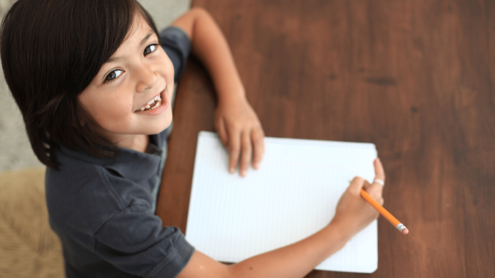 A girl smiling and writing in a notebook.