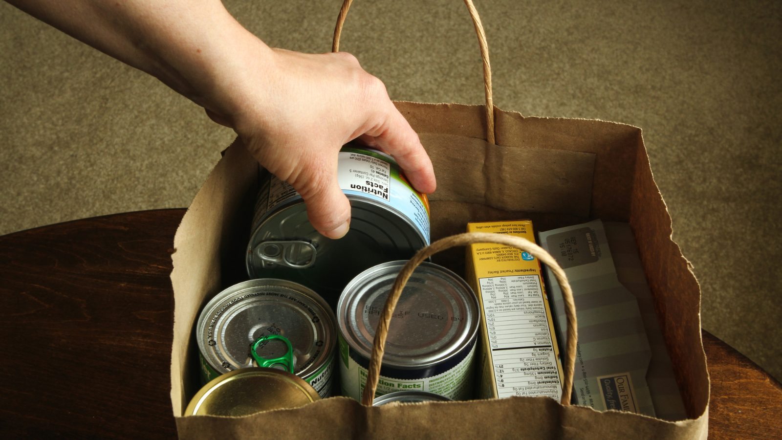 Someone placing canned food into a paper bag.
