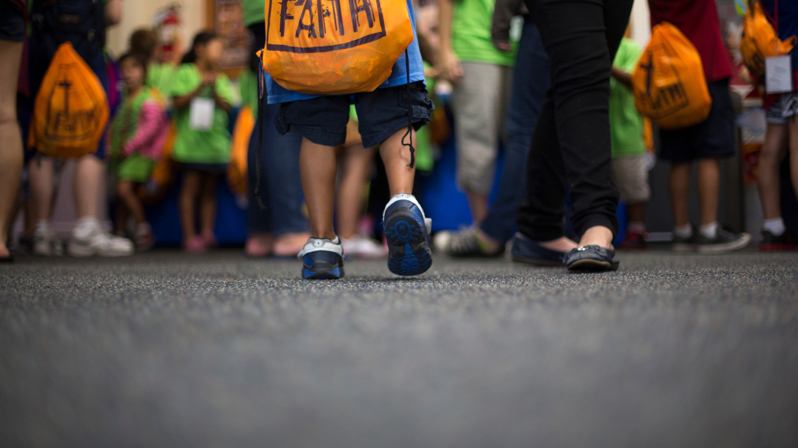 child carrying faith backpack in school crowd