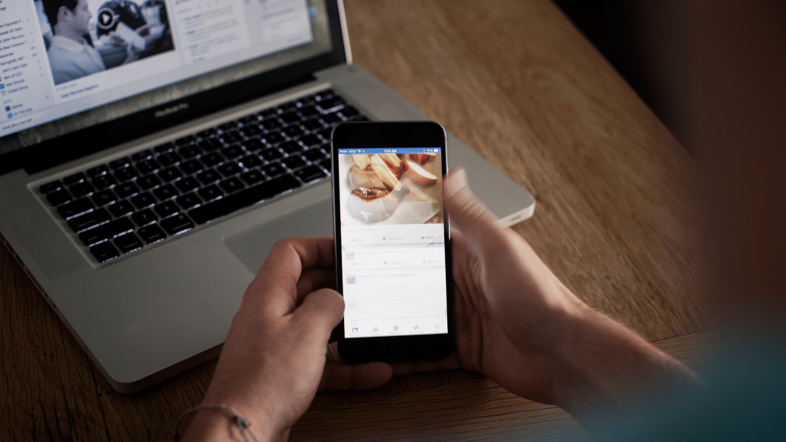 Hands holding a phone in front of a laptop.