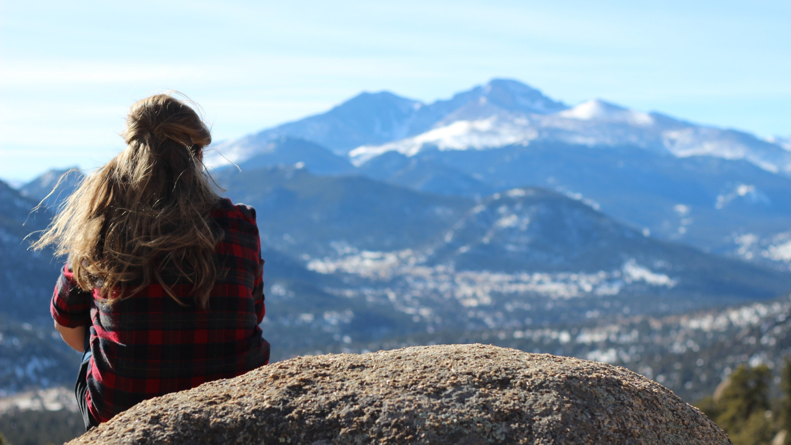 A woman sitting outside looking at mountains.