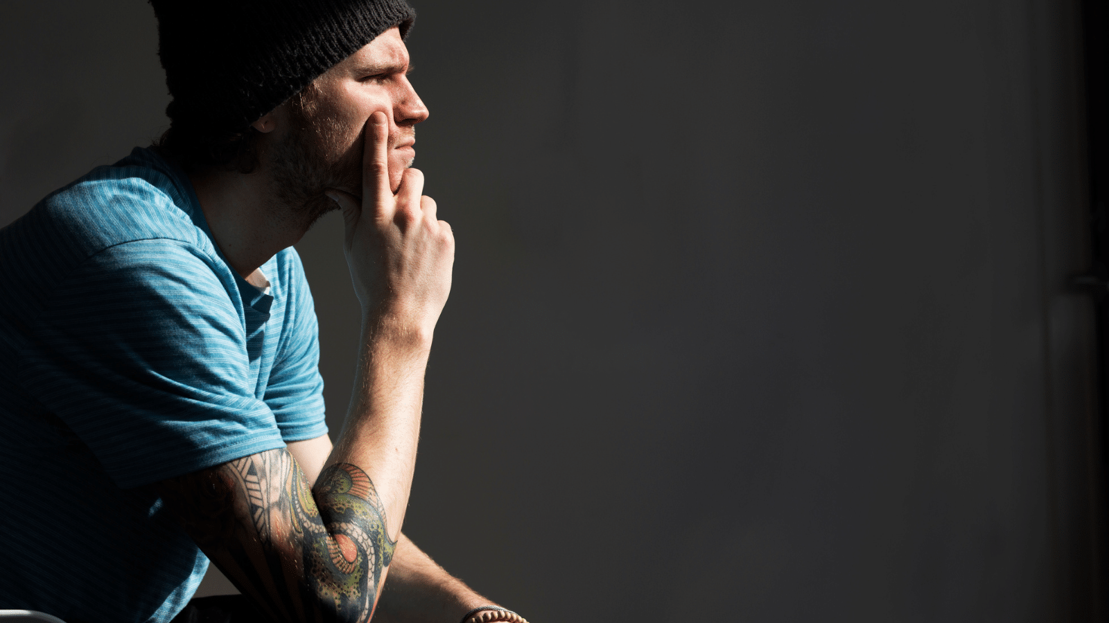 A man with tatoos sitting and thinking.