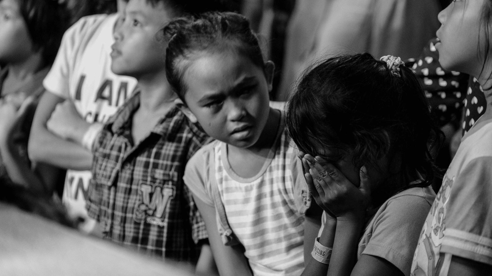 Children sitting at a table with one child crying while another child looks at her