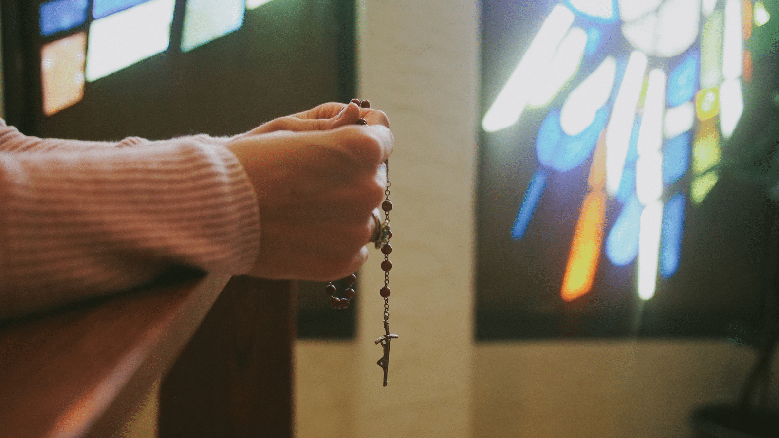Woman holding catholic rosary in front of a stained glass window