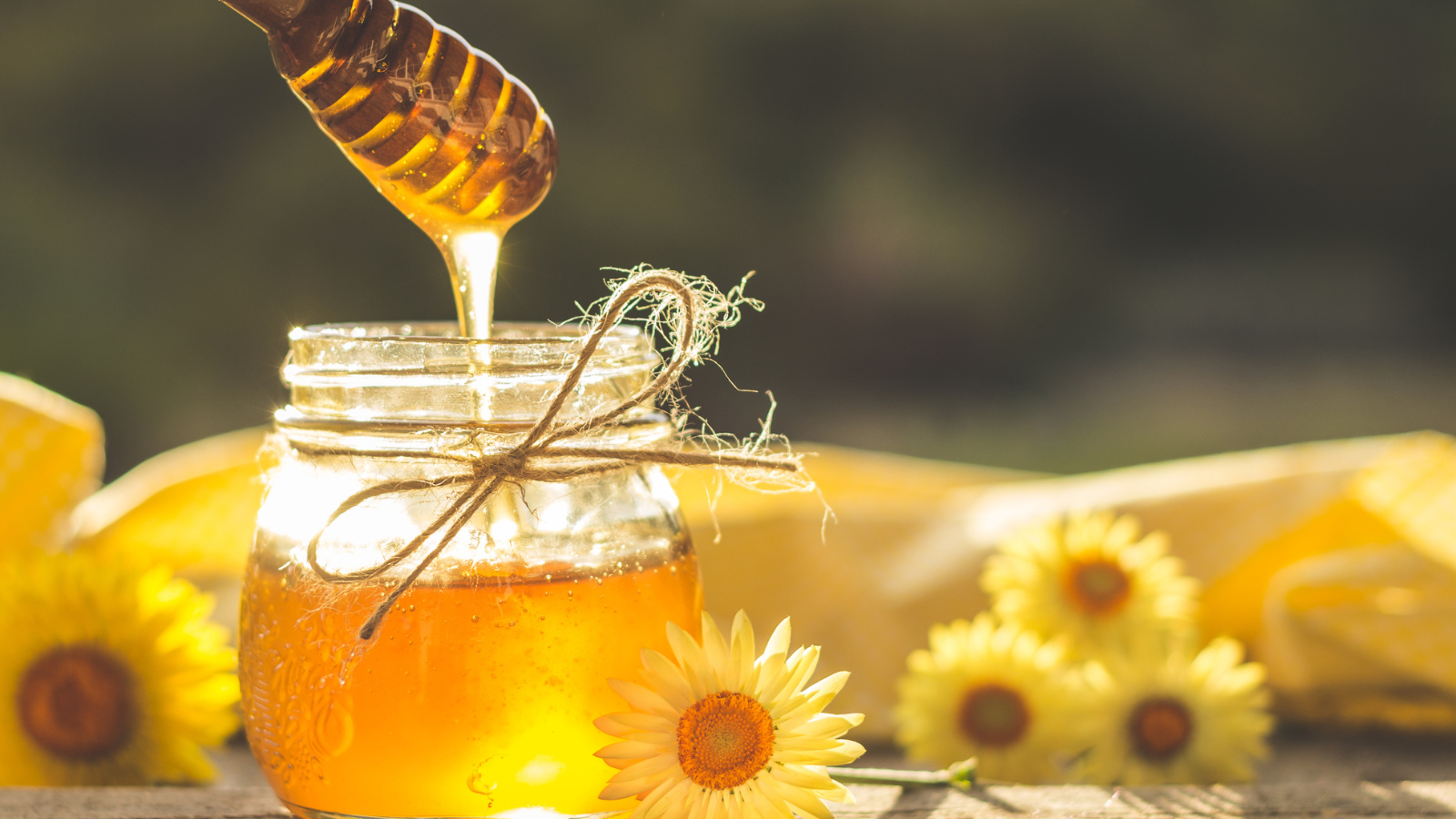 Glass jar of honey next to sunflowers