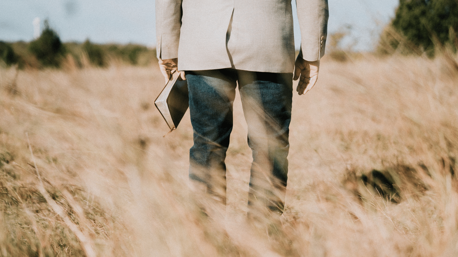 Man standing in a field with a Bible