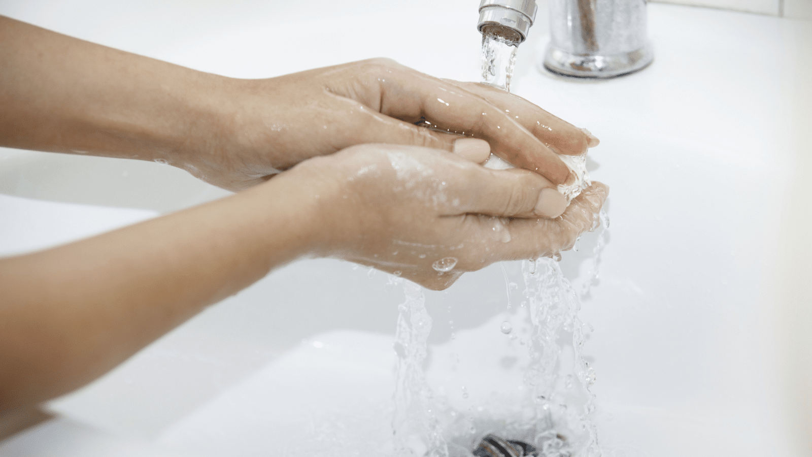 Two hands being washed in a white sink