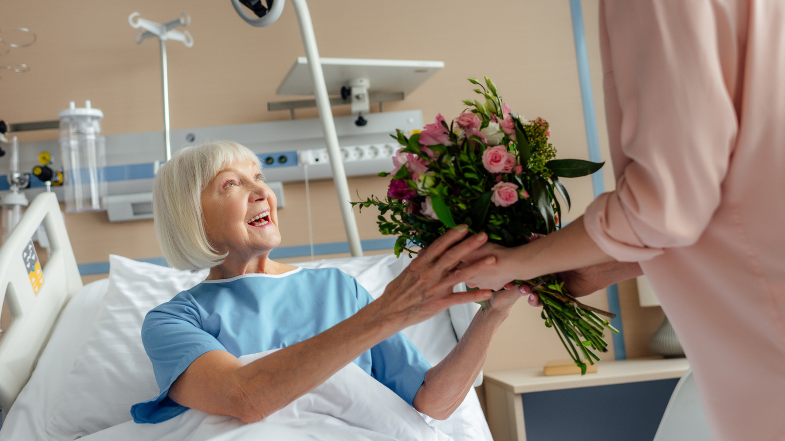Woman giving flowers to a patient in a hospital bed