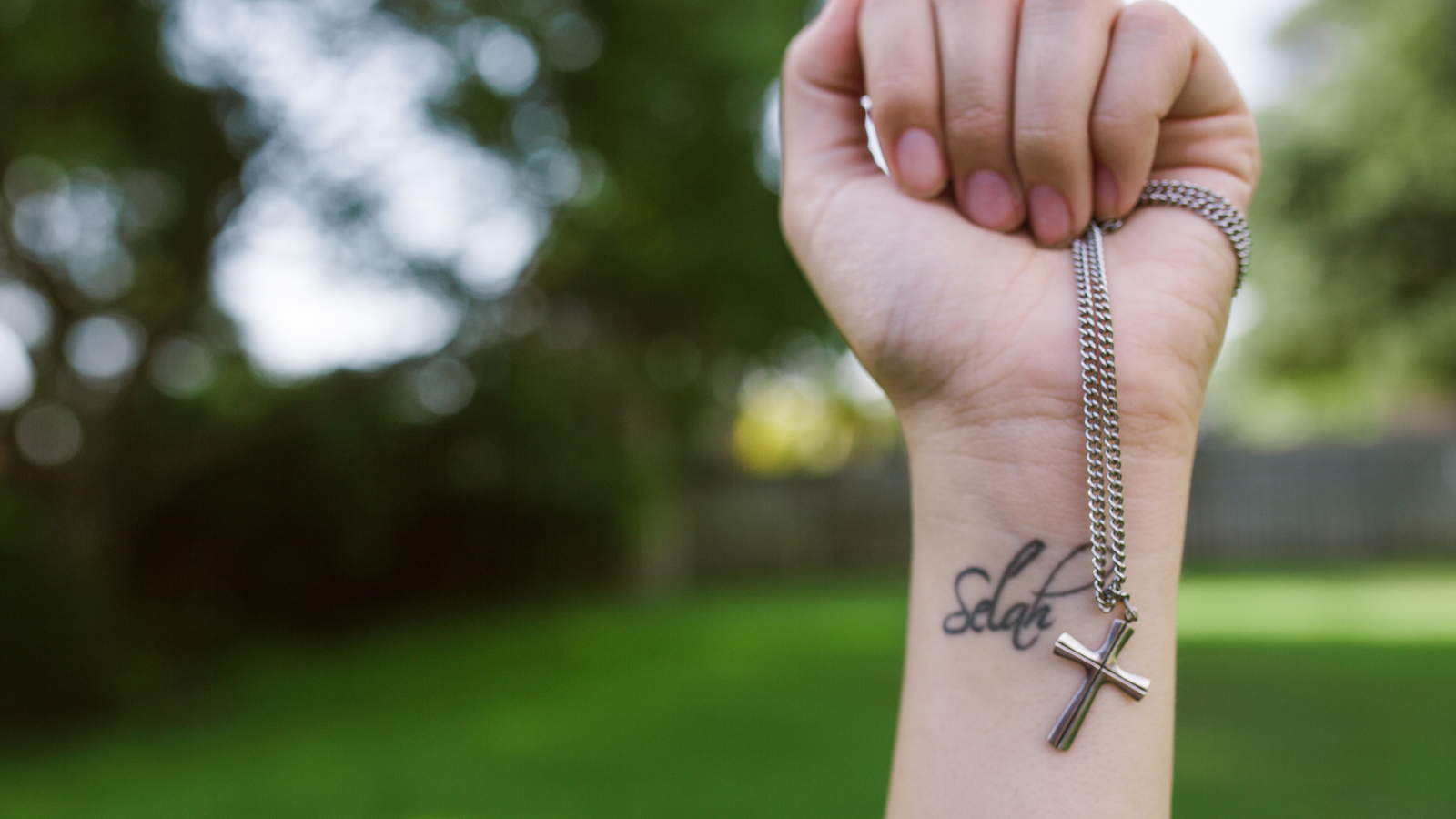 hand with selah tattoo holding cross necklace
