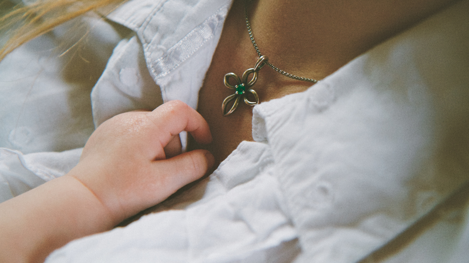 mom wearing cross necklace with baby hand