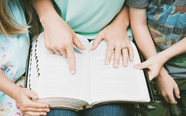 Mother pointing at a passage in Bible while sitting next to two kids
